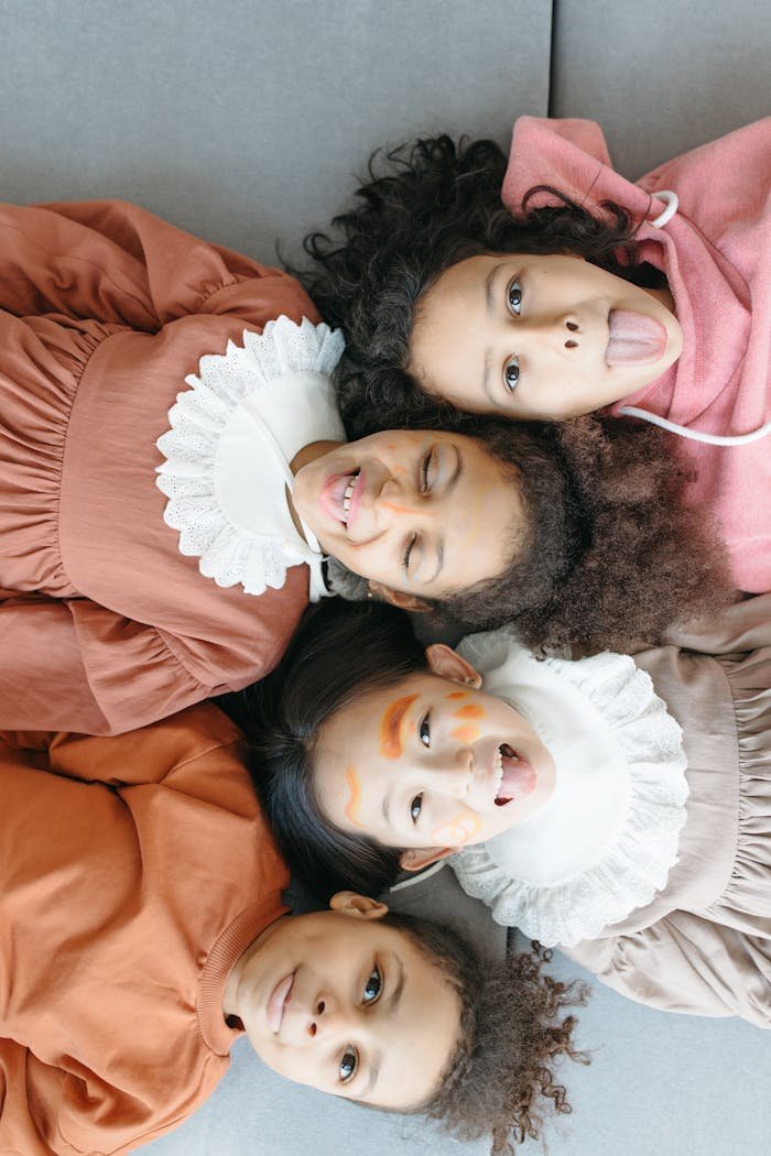 our-services-06 Four diverse children playfully posing on a gray sofa, expressing joy.