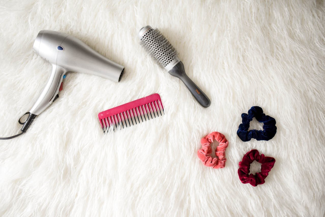portfolio-img-04 Flatlay of hairstyling tools including a hairdryer, brush, comb, and scrunchies on white fur.